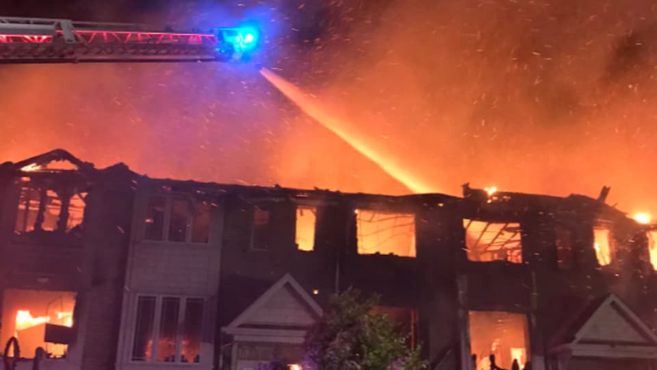 Les pompiers arrosent des maisons en flammes du haut d'une échelle.