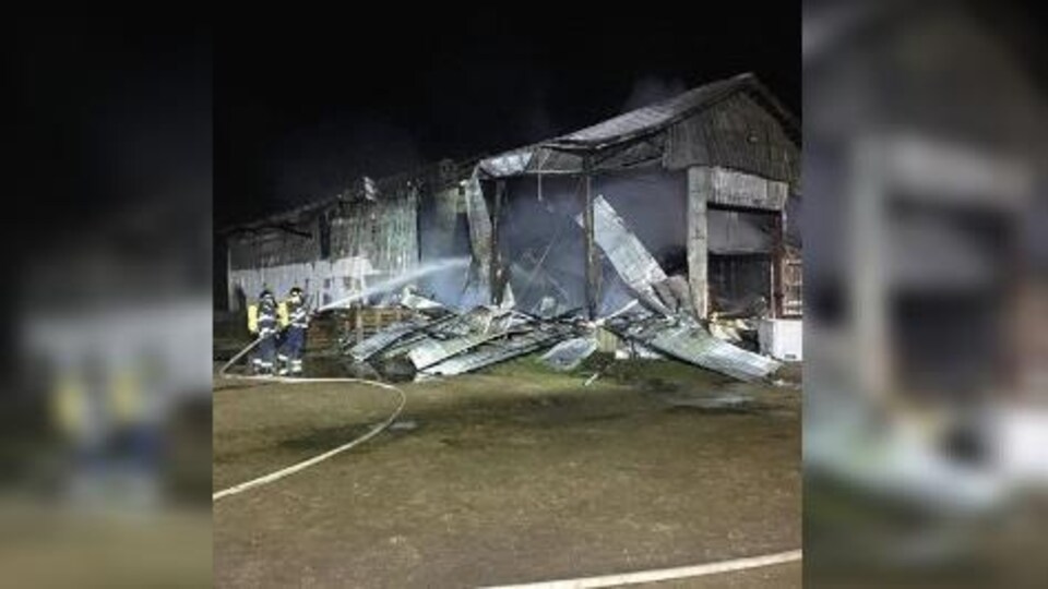 Deux pompiers arrosent une grange qui a été détruite par les flammes.