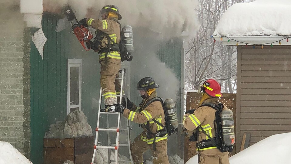 Trois hommes munis de casques, d'habits de pompier et de bombonnes d'oxygène interviennent sur le lieu de l'incendie.