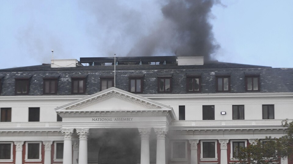 Des véhicules de pompiers devant le bâtiment d'où s'échappe une colonne de fumée.