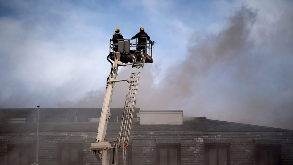 Deux pompiers sur une plateforme surélevée devant le bâtiment en feu. 