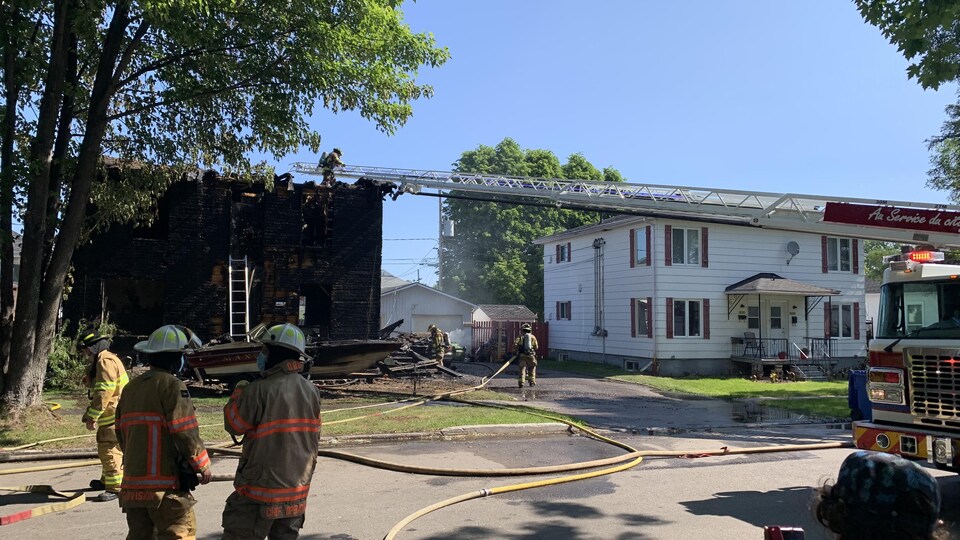Des pompiers devant une maison brûlée.