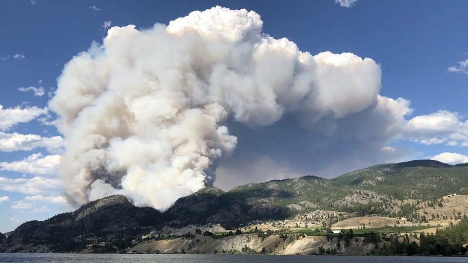 De la fumée s'échappe au-dessus d'une montagne près d'un lac.