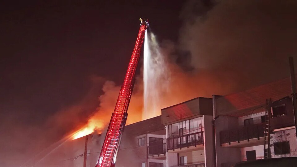 Un pompier sur une grande échelle au dessus d'un immeuble d'appartements en feu.