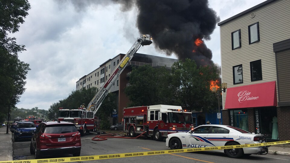 Flammes émanant d'un édifice entouré de véhicules d'urgence et de camion de pompiers.