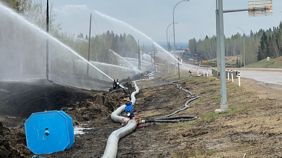 Un système de tuyaux pour éteindre les deux est installé le long d'une route à Drayton Valley, le 8 mai 2023 en Alberta.