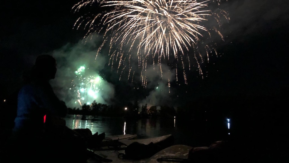 Un femme assise sur sa planche à pagaie regarde un feux d'artifice