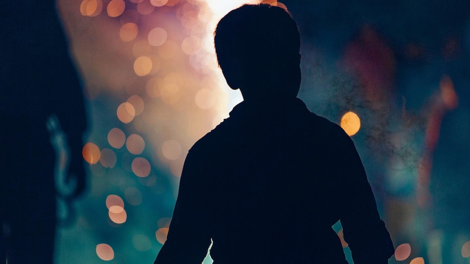 La silhouette d'une jeune garçon, et devant lui, la lumière d'un feu ou des petits feux d'artifice
