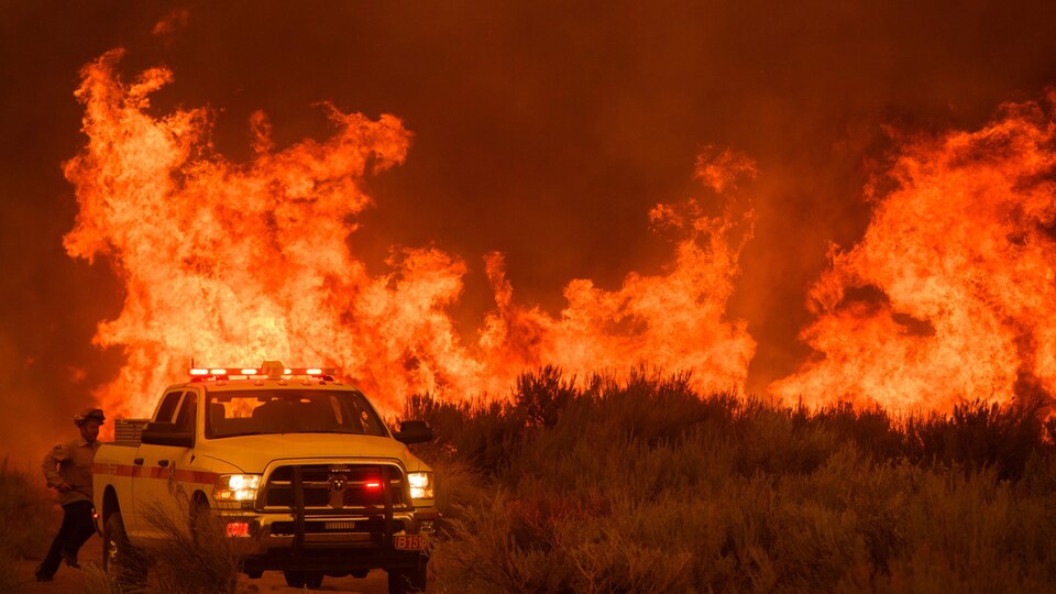 Un pompier court vers son camion alors que le feu avance vers une maison le 17 août 2021 près de Milford, en Californie.