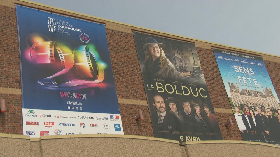 Trois affiches de cinéma de très grands formats sont accrochés côte à côte sur la façade extérieur d'un bâtiment.