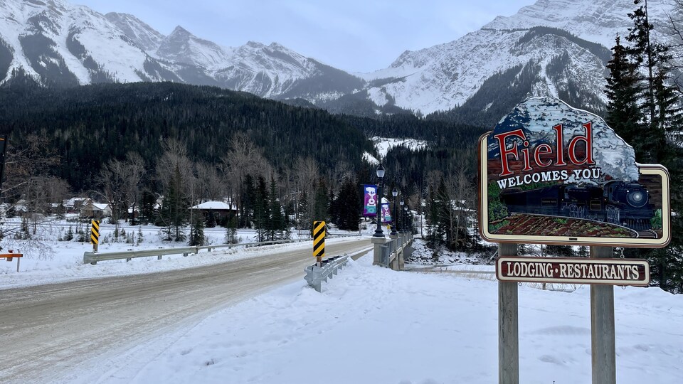 Une affiche près d'un pont annonce le village de Field dans un paysage montagnard et enneigé.
