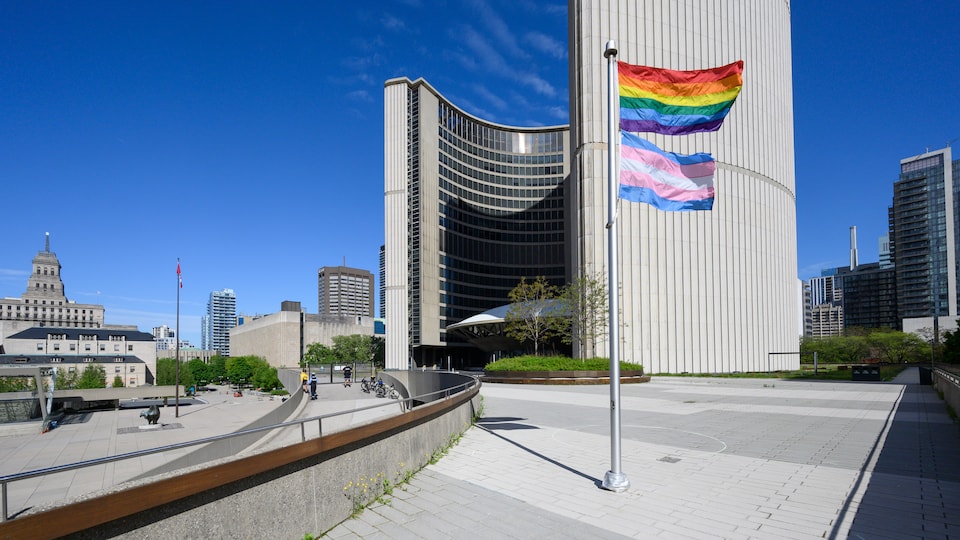 Les drapeaux arc-en-ciel et trans flottent à côté de l'hôtel de ville de Toronto.