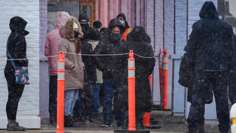 Des gens masqués attendent dans une file d'attente.