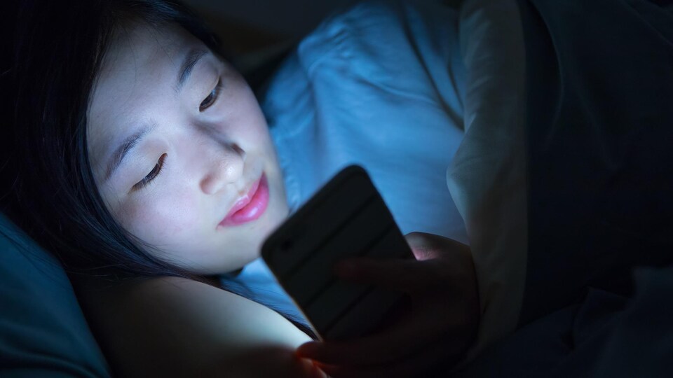 Une jeune fille regarde son téléphone dans son lit.