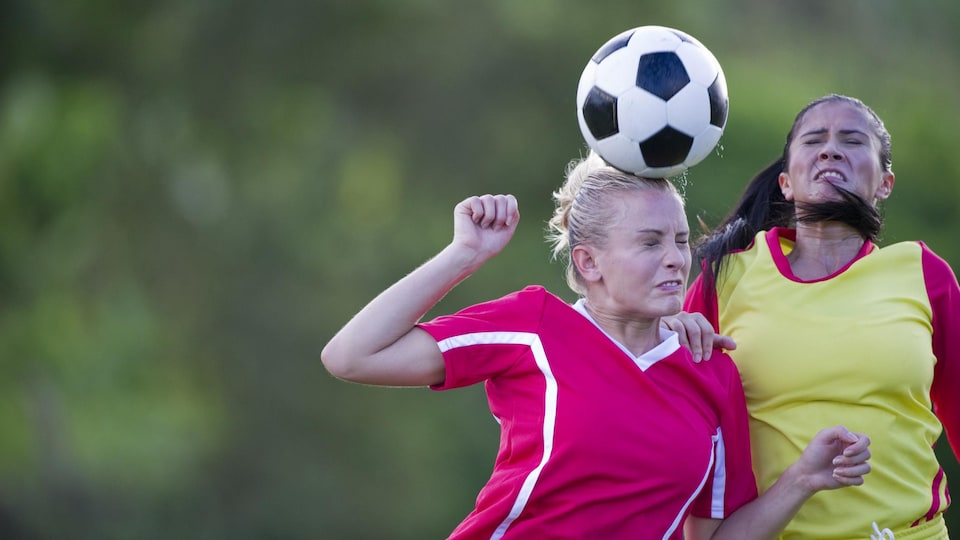 Une jeune femme frappe un ballon de soccer avec la tête. 