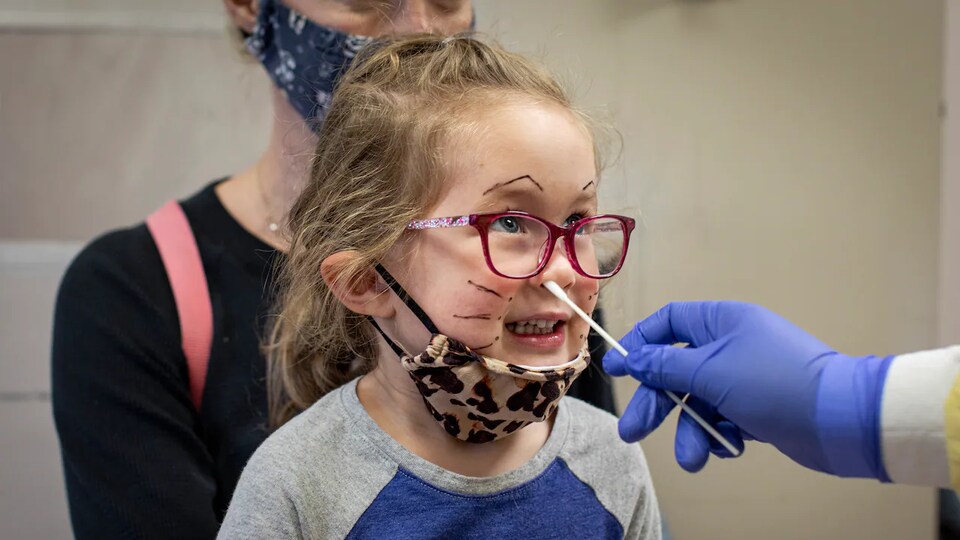 Une personne entre un écouvillon dans le nez d'une petite fille pour lui faire passer un test de dépistage de la COVID-19.