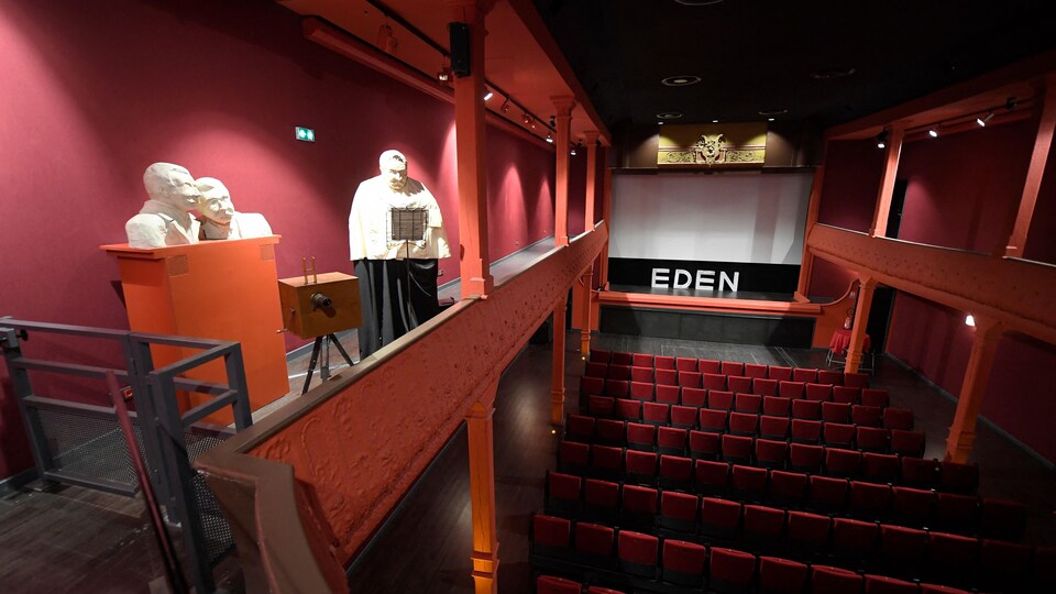 Une salle de cinéma. Une statue des frères Lumière est installée sur la mezzanine de la salle.