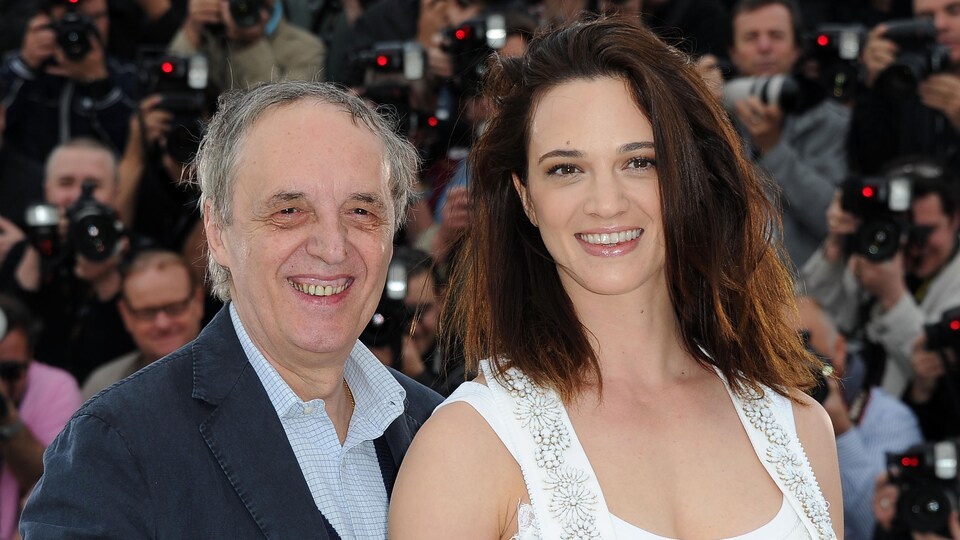 Un homme et une femme tout sourire posent sur le tapis rouge à Cannes entourés d'un important groupe de photographes. 