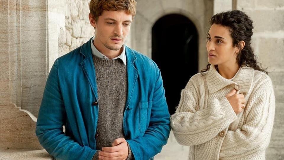 Un jeune homme et une jeune femme sont debout l'un à côté de l'autre devant un bâtiment de pierre.