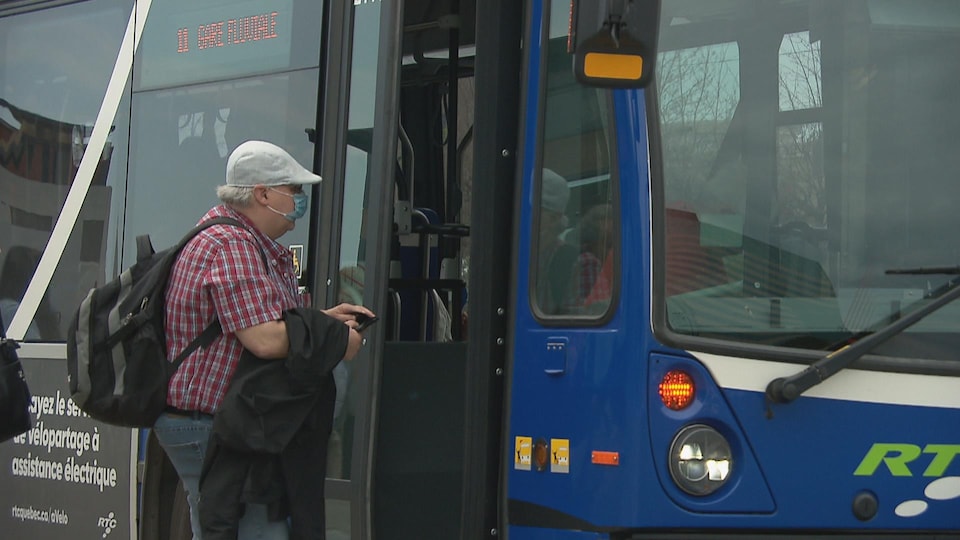 Un homme avec une casquette et un masque sur le visage monte dans un bus par la porte avant.