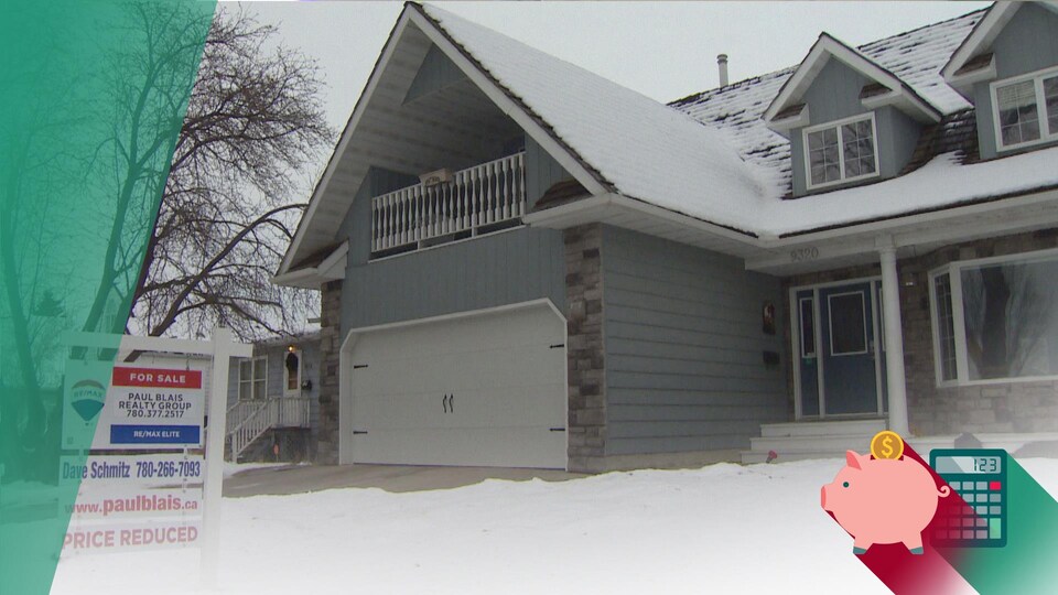 Une maison grise recouverte de neige. Devant la maison, une pancarte qui indique que son prix a été réduit.