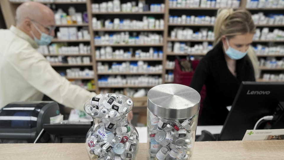 Deux employés s'affairent derrière des contenants remplis de fioles de vaccin vides dans une pharmacie.