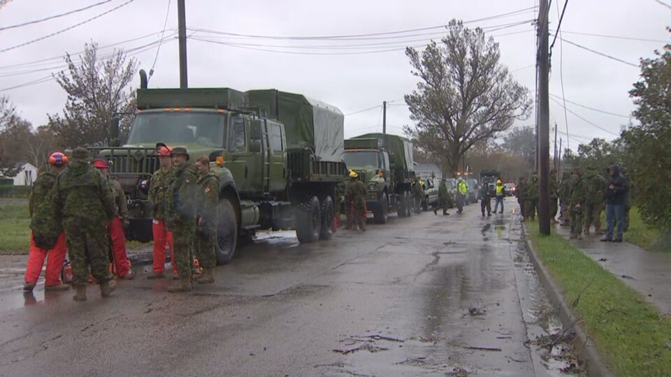 Des soldats sont regroupés près de leurs camions dans une rue en compagnie de travailleurs civils.
