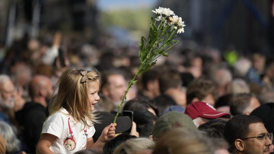 Une jeune fille tient des fleurs dans la foule.