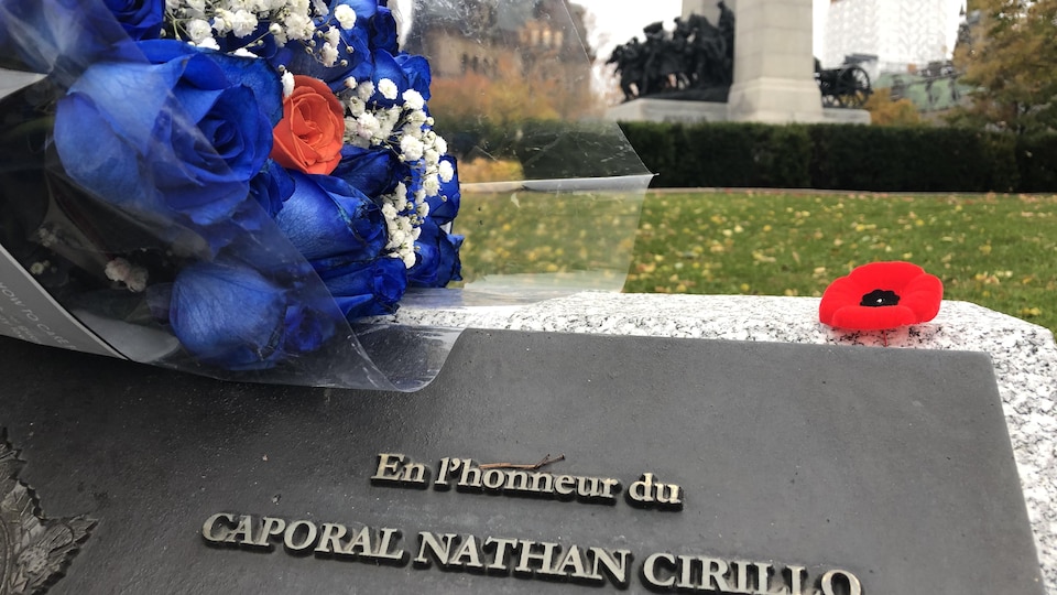 Un bouquet de roses bleues est déposé sur la plaque, avec le monument en arrière-plan.