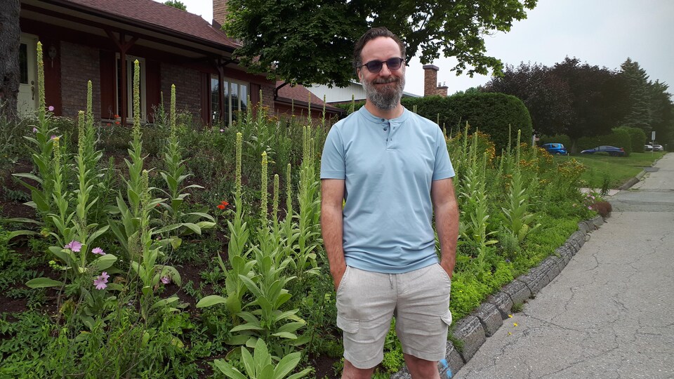 Dany Baillargeon devant sa résidence, où l'on trouve de nombreuses fleurs.