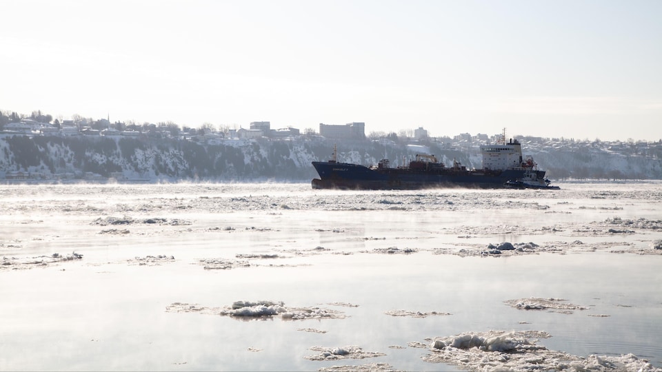 Un bateau de transport est sur le fleuve plein de glace et de vapeur, causées par le froid. 