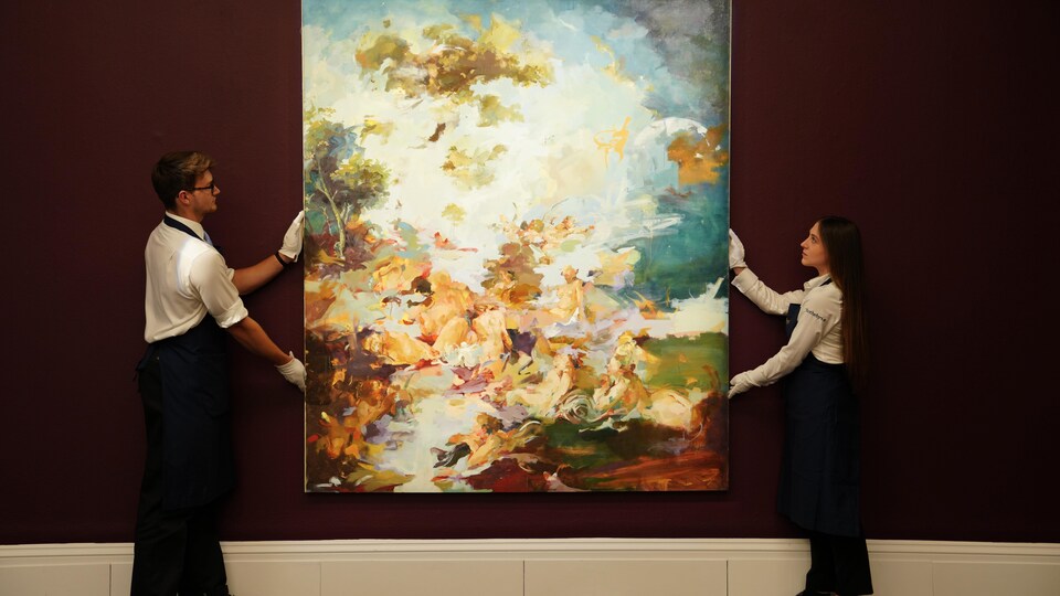 Un homme et une femme installés de chaque bord d'une grande toile la tiennent avec des mains gantées, afin de l'accrocher sur un mur bourgogne. 