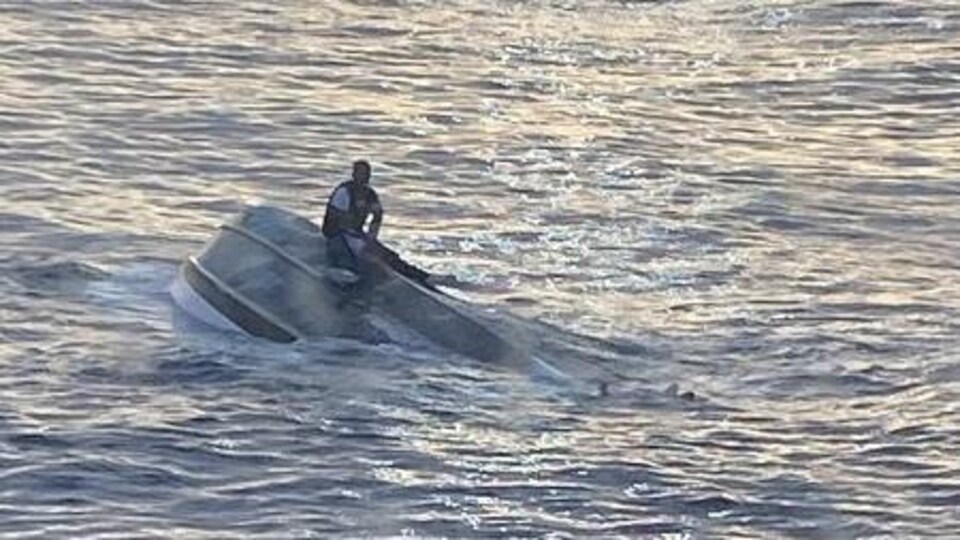 Un homme assis sur un bateau chaviré.