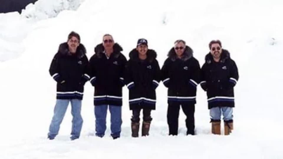 Cinq hommes vêtus d'anorak se tiennent côte à côte, debout dans la neige.