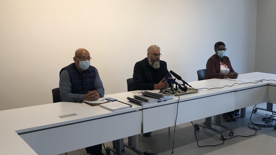 Une femme et deux hommes en conférence de presse.