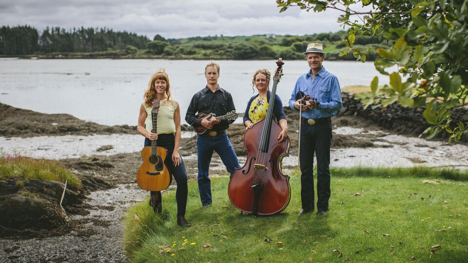 Les quatre membres du groupe The Foghorn Stringband posent près d'un lac avec leurs instruments.