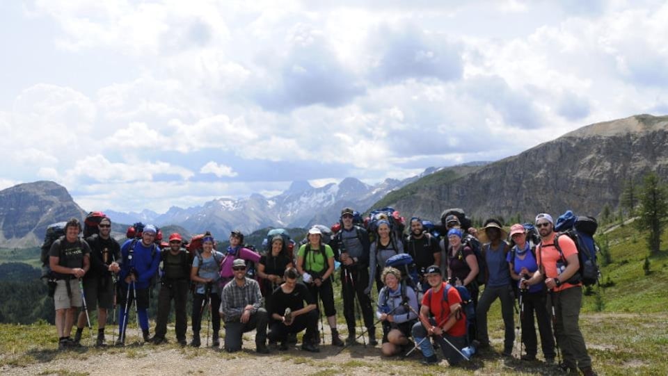 Un groupe de jeunes est réuni pour prendre une photo au sommet d'une montagne. À l'arrière, on voit les Rocheuses canadiennes. 