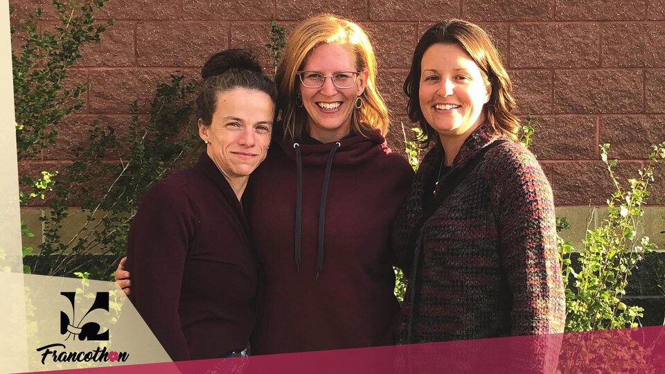 Trois femmes sont bras dessus, bras dessous devant un mur où apparaît le nom de l'école Nouvelle-frontière.