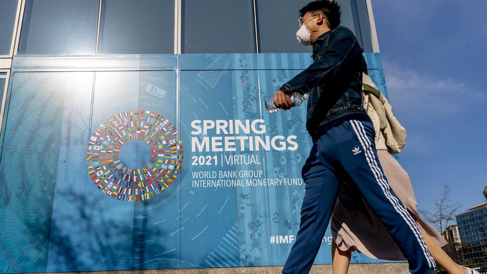 Deux passants à l'extérieur, devant un un poster qui annonce le sommet virtuel tenu par le Fonds monétaire international et la Banque mondiale.