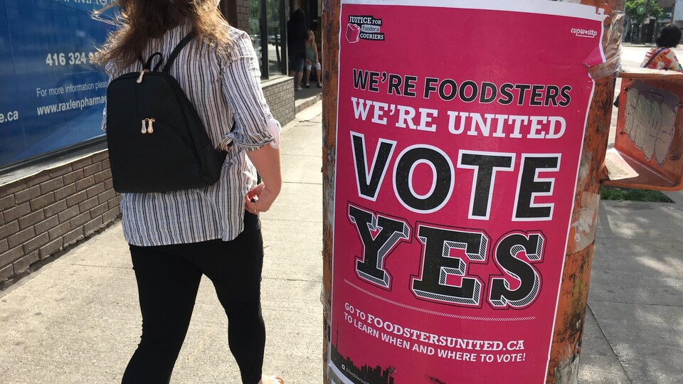 Une piétonne devant affiche rose où il est écrit votez oui.