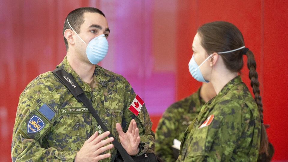 Deux militaires discutent ensemble. Ils portent un masque.