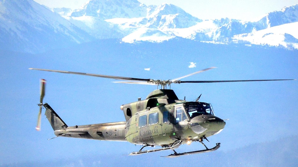 Un hélicoptère de l'armée canadienne en plein vol devant des montagnes.