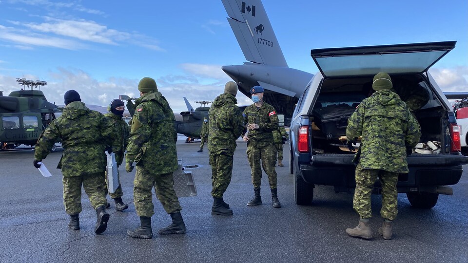 Des militaires en uniforme transportent de l'équipement depuis une camionnette vers des hélicoptères et un avion.