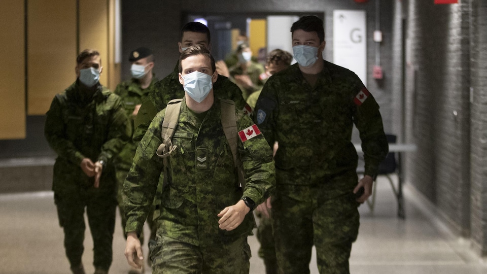 Des militaires des Forces armées canadiennes portant un masque dans un couloir d'un collège.