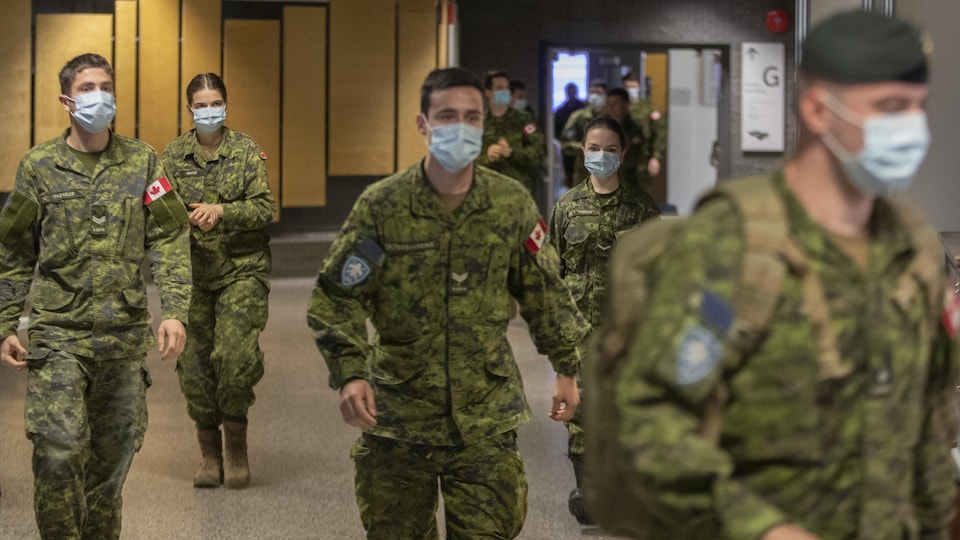 Des militaires portant un masque marchent dans un édifice.