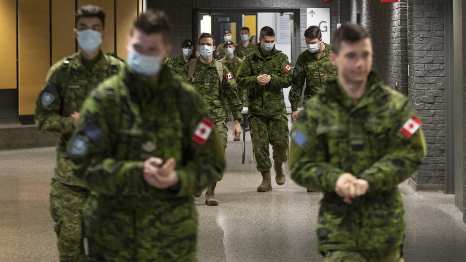 Des militaires des Forces armées canadiennes, la plupart portant un masque.  