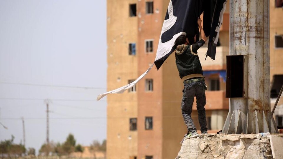 Un membre des FDS retire un drapeau du groupe armé État islamique à Tabqa, le 30 avril.