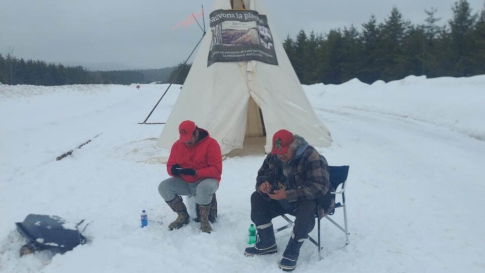 Édouard Chilton et Steven sont sur leurs téléphones devant un tipi. 