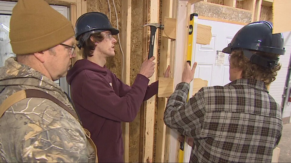 Deux jeunes hommes installent une porte dans une maison en construction.