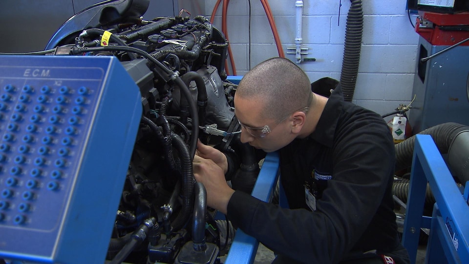 Un homme répare un moteur. Il porte des lunettes de protection.